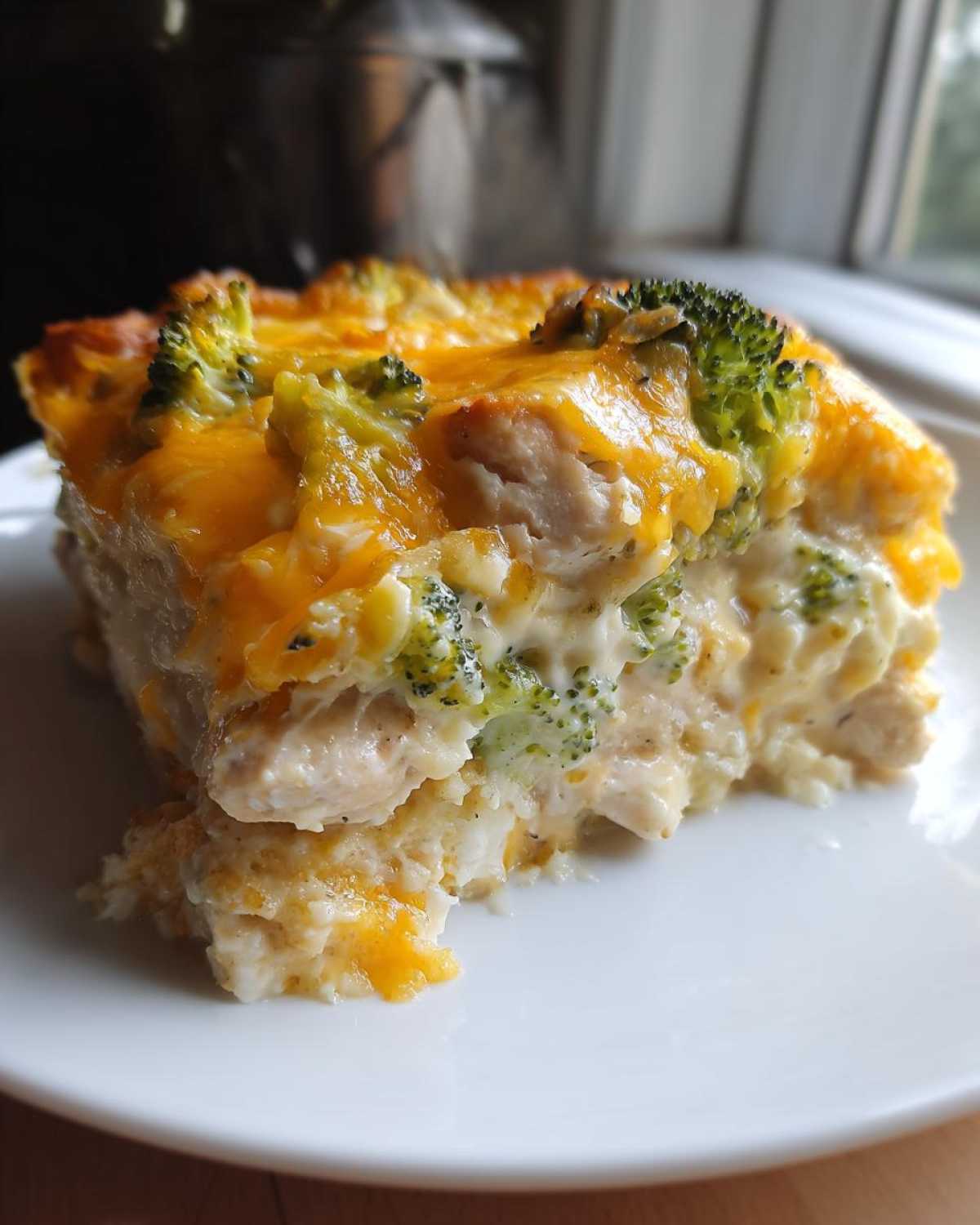 A thick, creamy slice of Chicken Divan casserole topped with melted cheddar cheese and broccoli florets.