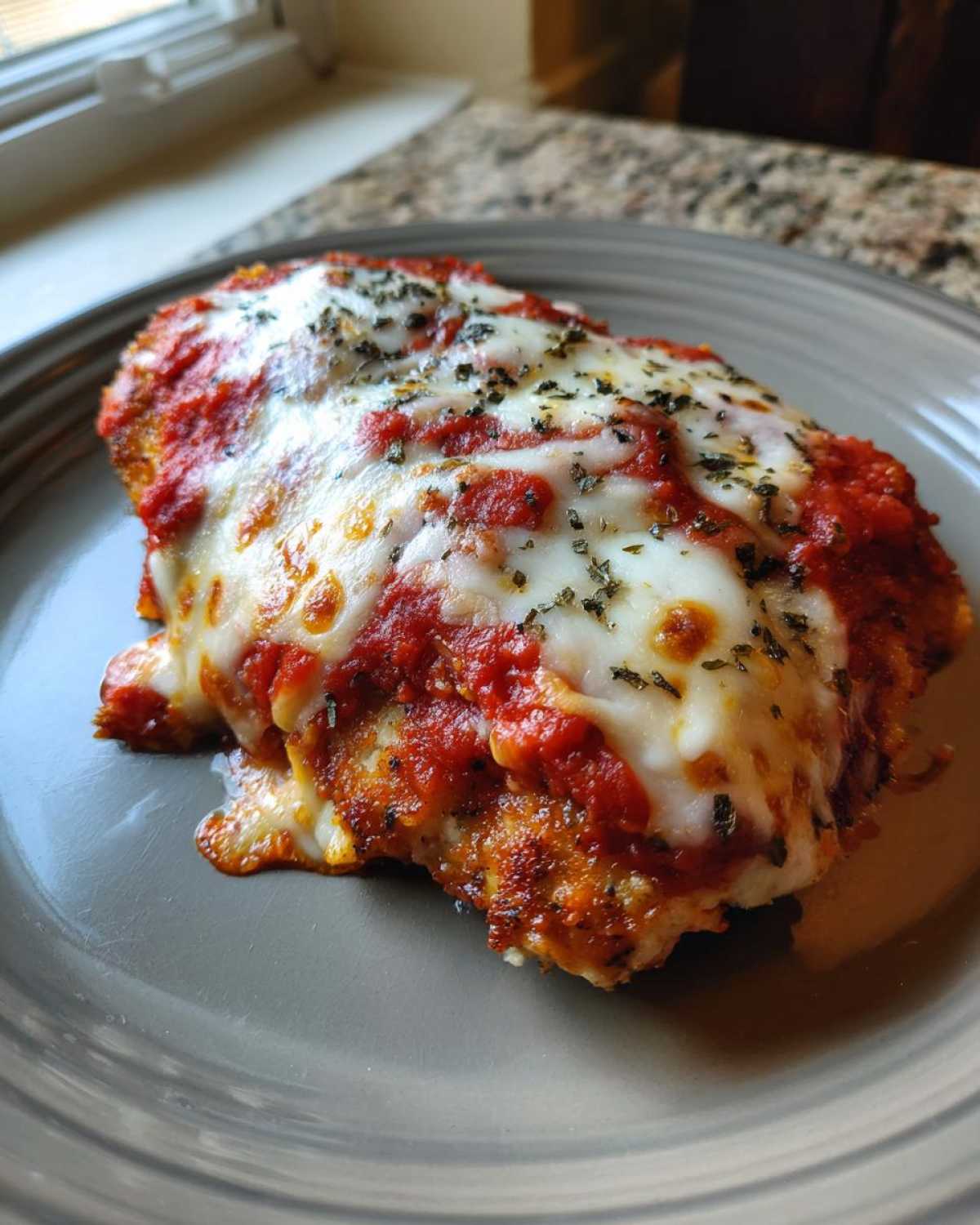 A close-up of a single serving of golden-brown chicken parmesan recipe topped with melted mozzarella and marinara sauce.