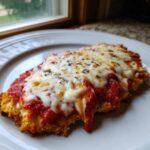 A close-up of a crispy, breaded chicken parmesan recipe cutlet topped with melted mozzarella and marinara sauce.