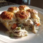 A serving of creamy chicken pot pie casserole topped with golden biscuits, showing shredded chicken and vegetables.