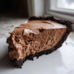 Close-up of a thick slice of chocolate mousse pie showing the airy filling and dark cookie crust.