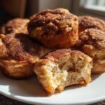 A plate of freshly baked cinnamon sugar french toast muffins, one of which has a bite taken out showing the soft interior.