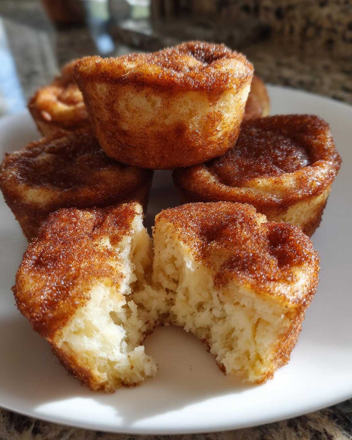 A stack of golden cinnamon sugar french toast muffins, with one broken in half showing the soft interior.
