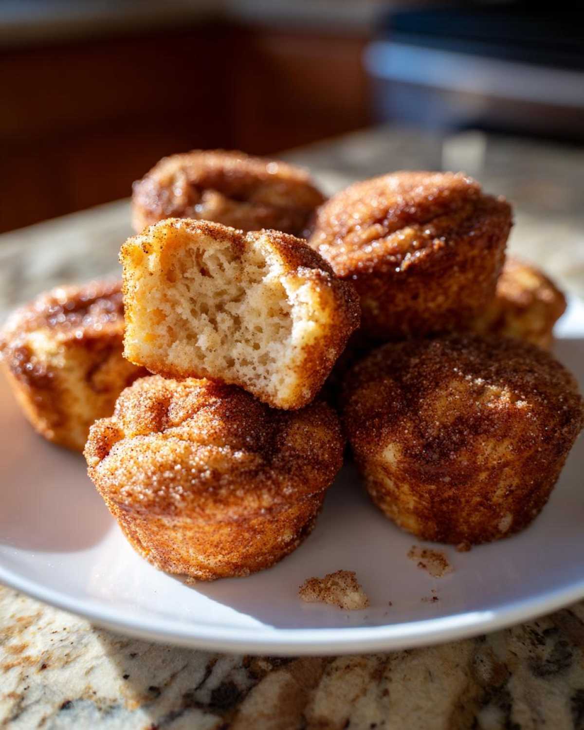A stack of golden brown cinnamon sugar french toast muffins, one broken open to show the fluffy interior.