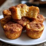A stack of freshly baked cinnamon sugar french toast muffins, one broken open showing the fluffy interior.