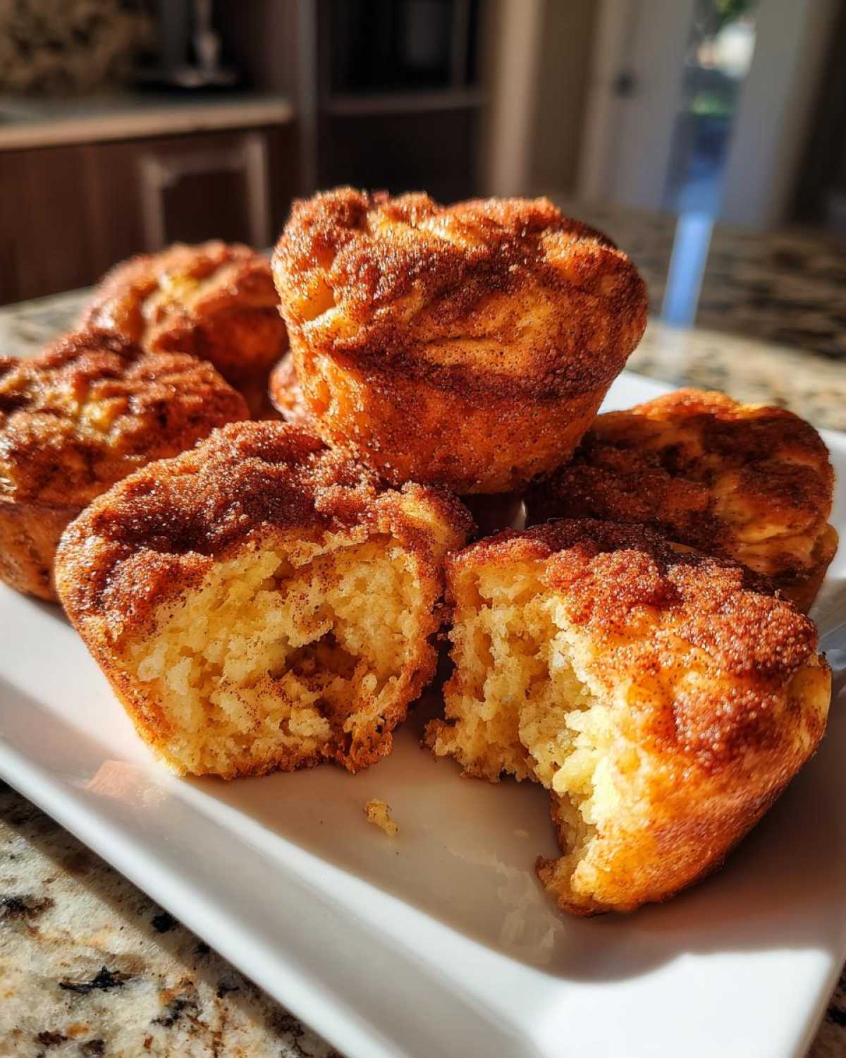 A stack of golden cinnamon sugar french toast muffins, one broken open to show the soft interior.