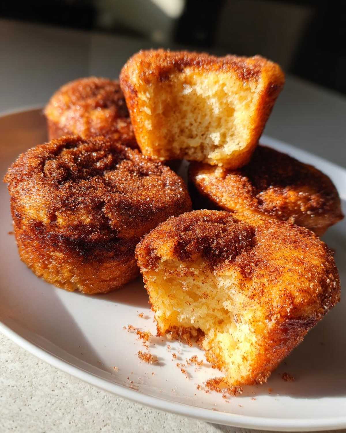 A stack of golden cinnamon sugar french toast muffins, one broken open to show the fluffy interior.
