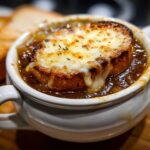 Close-up of a bowl of rich french onion soup topped with a thick slice of bread and bubbly, melted Gruyère cheese.