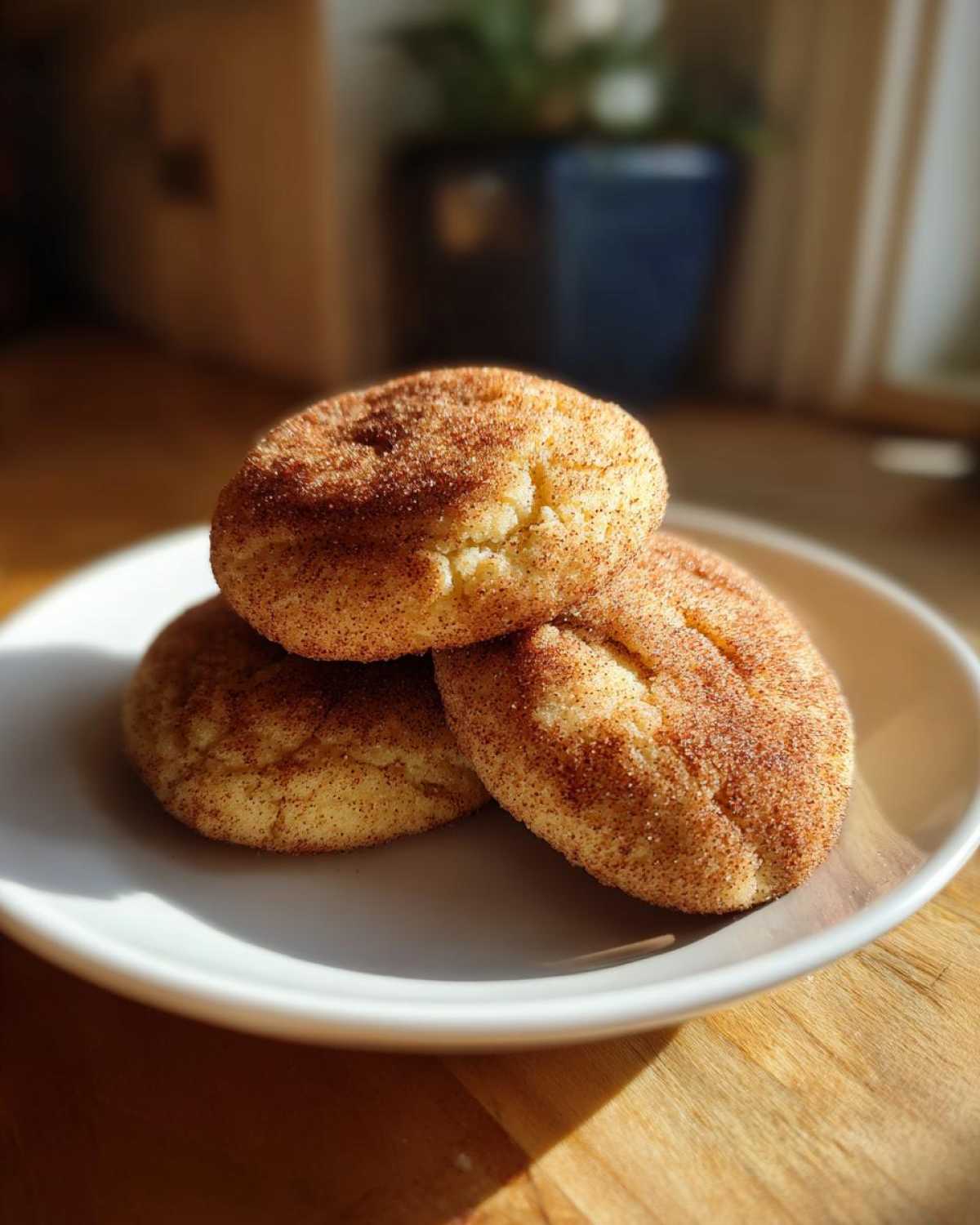 Three soft, chewy snickerdoodles coated in cinnamon sugar stacked on a white plate.