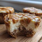 Close-up of a cookie butter cheesecake cup with a bite taken out, drizzled with caramel sauce.
