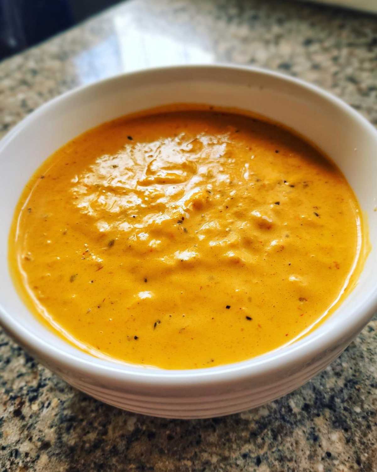 A close-up shot of rich, orange beer cheese dip served warm in a small white bowl.