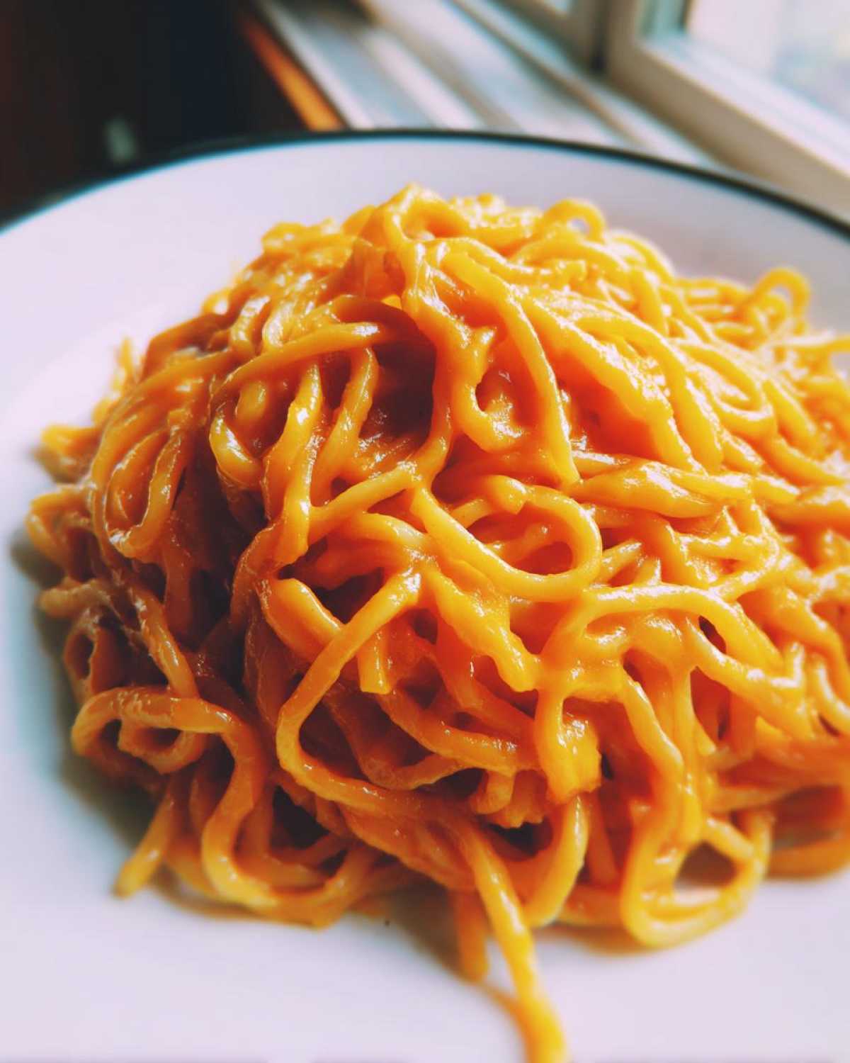 Close-up of spaghetti noodles generously coated in a vibrant orange butternut squash pasta sauce.