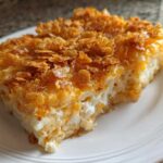 A close-up of a serving of cheesy potato casserole topped with crispy, golden cornflakes.