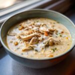Close-up of a bowl of creamy white chicken chili topped with shredded chicken and a swirl of cream.