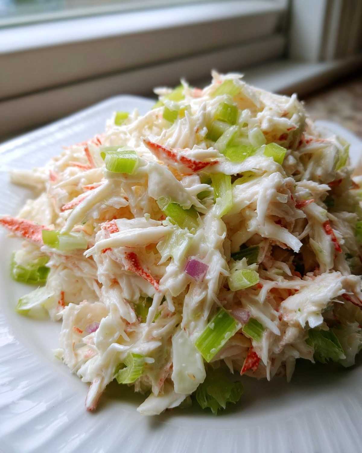 A mound of creamy crab salad made with shredded imitation crab, celery, and a light dressing, served on a white plate.