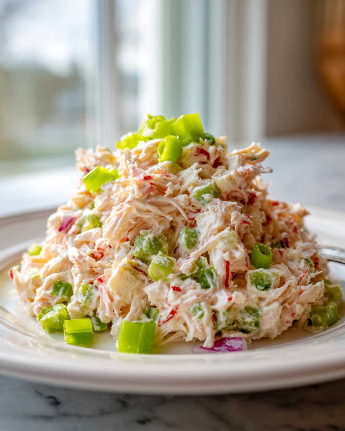 A mound of creamy crab salad mixed with celery and red onion, topped with bright green scallions.