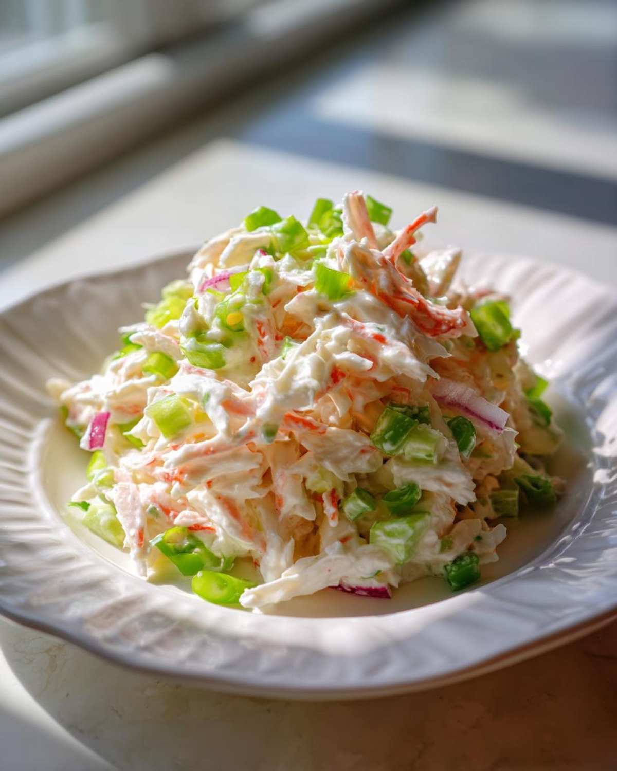 A mound of creamy crab salad mixed with chopped green celery and red onion served on a white plate.