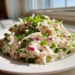 A mound of creamy crab salad mixed with red onion and topped generously with chopped green onions.