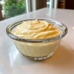 A small glass bowl filled with thick, creamy, pale yellow homemade garlic aioli.