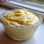 A close-up of thick, pale yellow homemade garlic aioli served in a small, ribbed glass bowl.