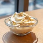 A small glass bowl filled with thick, freshly whipped creamy horseradish sauce sitting on a wooden table.