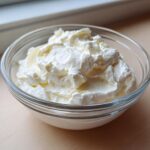 Close-up of thick, fluffy white creamy horseradish sauce served in a small, clear glass bowl.