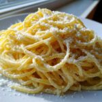 A close-up shot of a mound of creamy lemon pasta topped generously with grated white cheese.