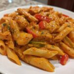 Close-up of creamy, orange-sauced Rasta Pasta with chunks of chicken and colorful bell peppers.