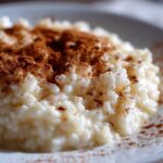Close-up of creamy rice pudding recipe served in a white bowl and generously dusted with ground cinnamon.