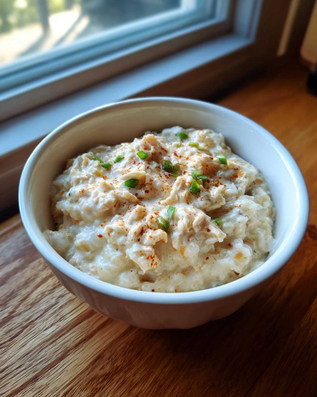 A close-up of creamy white chicken chili topped with paprika and green onions in a white bowl.