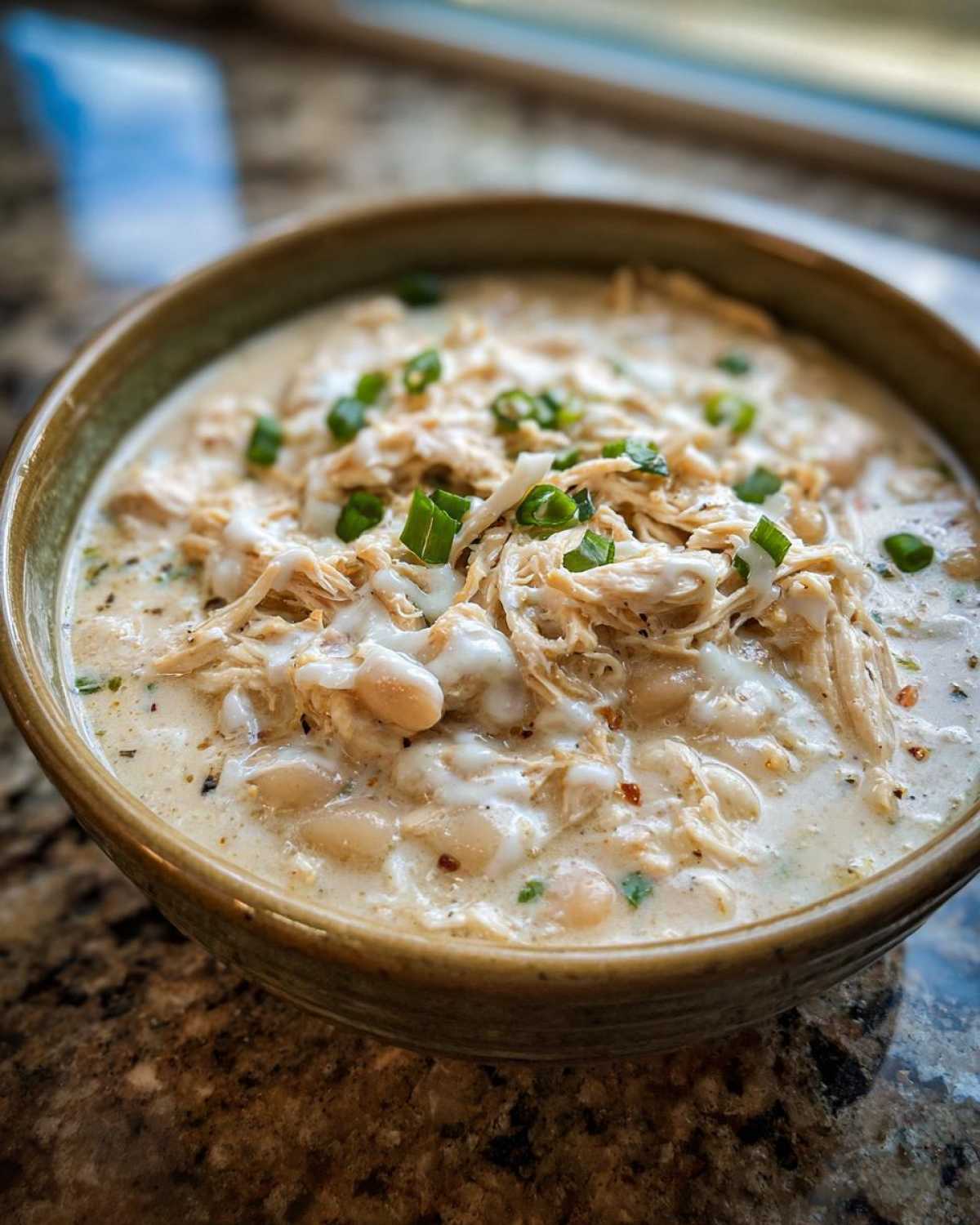 Close-up of a creamy white chicken chili bowl, featuring shredded chicken, white beans, and green onion garnish.