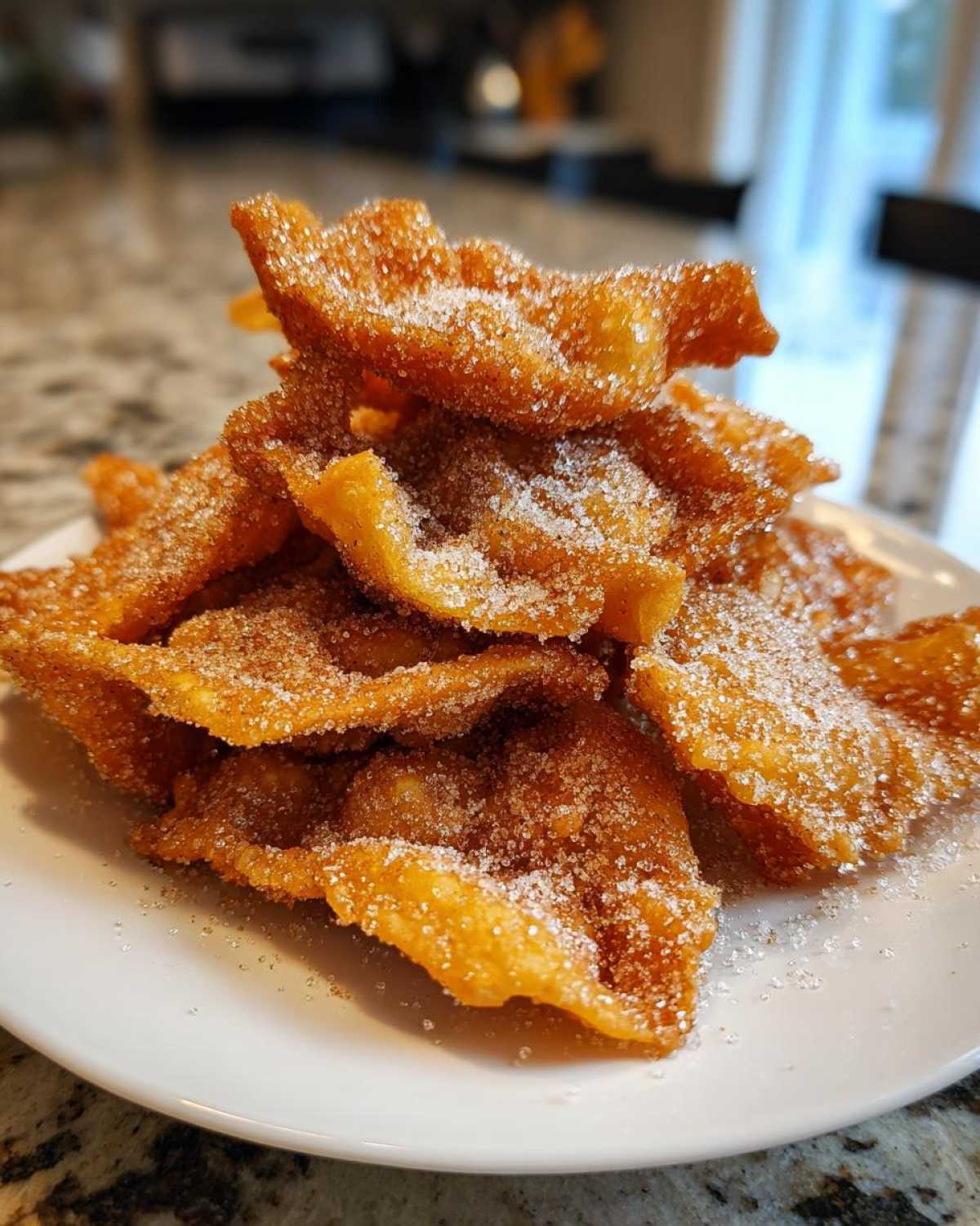 A close-up of a pile of golden, crispy buñuelos generously dusted with granulated sugar.