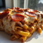 A close-up, featured shot of a hearty slice of pizza pasta bake topped with melted mozzarella and pepperoni slices.