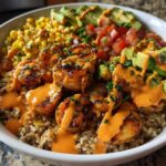 Overhead view of a vibrant shrimp bowl featuring seasoned shrimp, brown rice, corn, avocado, and a creamy orange sauce.
