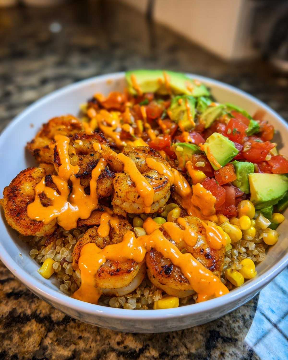 Close-up of a flavorful shrimp bowl featuring seasoned shrimp, quinoa, avocado, salsa, and a drizzle of orange sauce.