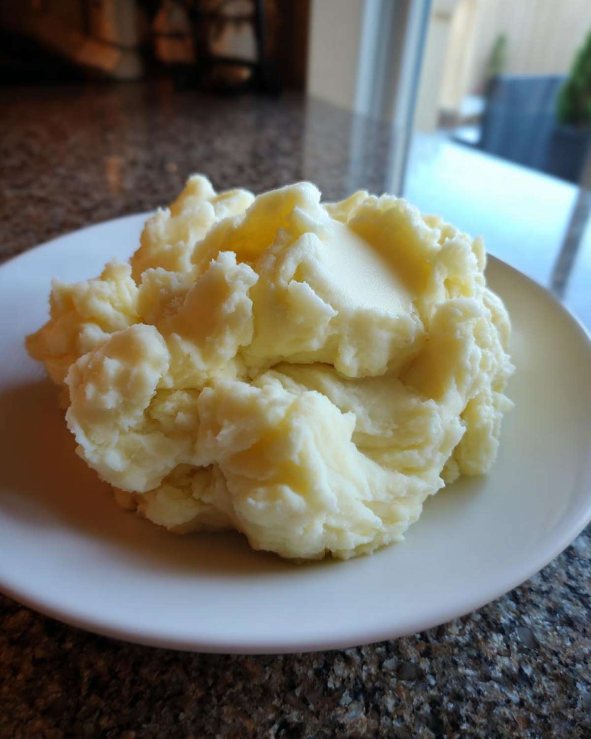 A generous serving of creamy, fluffy mashed potatoes topped with a pat of melting butter on a white plate.