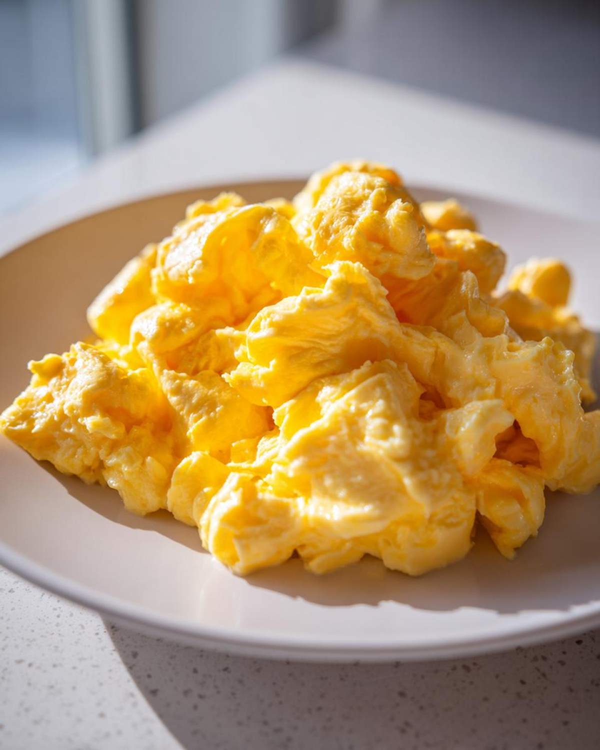 A close-up of a generous serving of bright yellow, fluffy scrambled eggs piled high on a white plate.