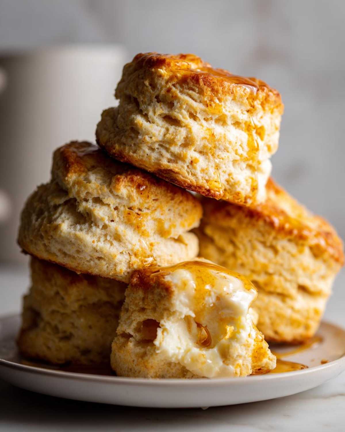 A stack of fluffy sweet potato biscuits drizzled with honey, one split open with butter.