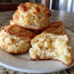 A stack of golden brown sweet potato biscuits, one split open showing melted butter inside.