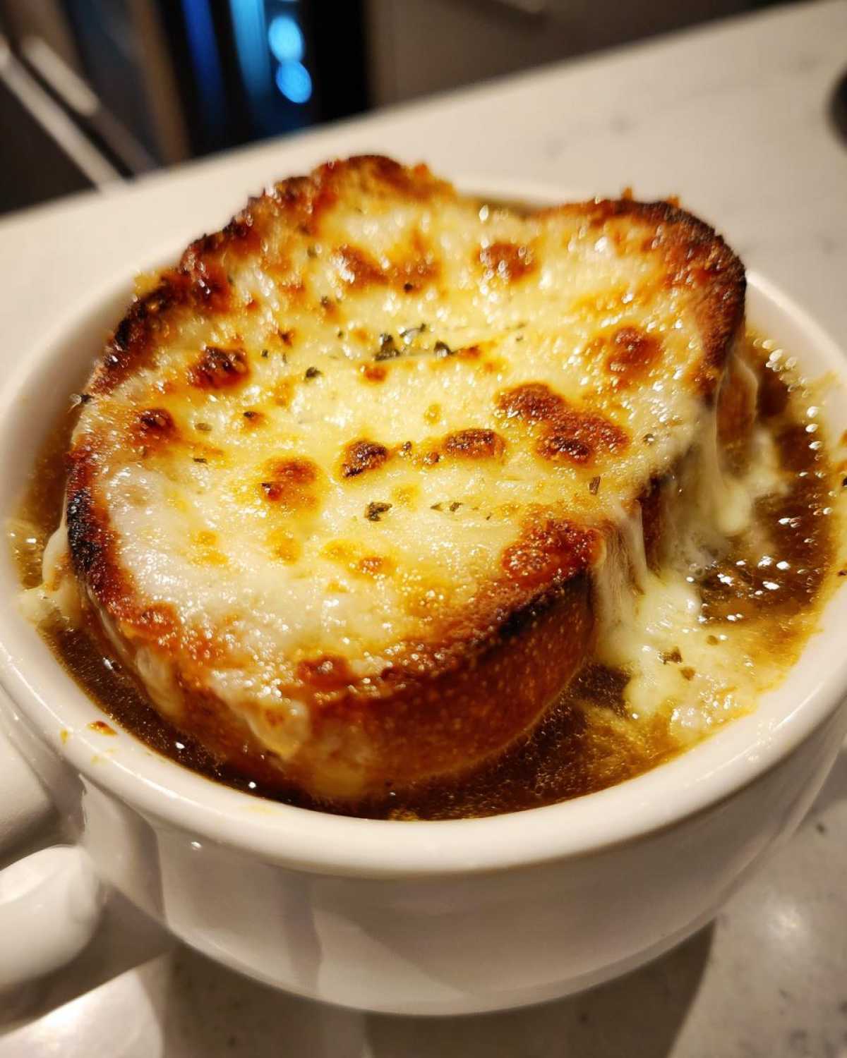 Close-up of a white bowl filled with rich french onion soup topped with a thick layer of melted, browned cheese over crouton.