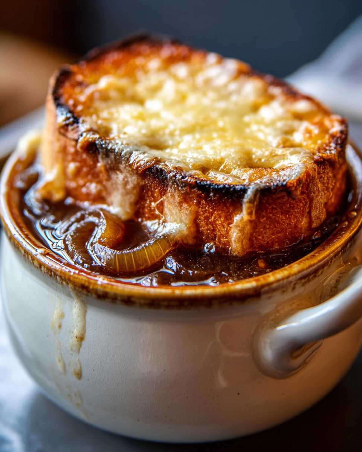 Close-up of rich french onion soup topped with a large crouton covered in melted, browned cheese.