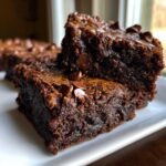 Close-up of two fudgy gingerbread brownies stacked on a white plate, topped with chocolate chips.