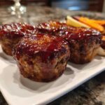 Four individual mini meatloaf portions topped with a thick, shiny glaze, served alongside roasted root vegetables.