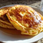 A stack of three golden brown coconut flour pancakes drizzled with syrup and topped with melting butter.