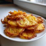A close-up of a pile of golden brown, thinly sliced fried potatoes served on a white plate.