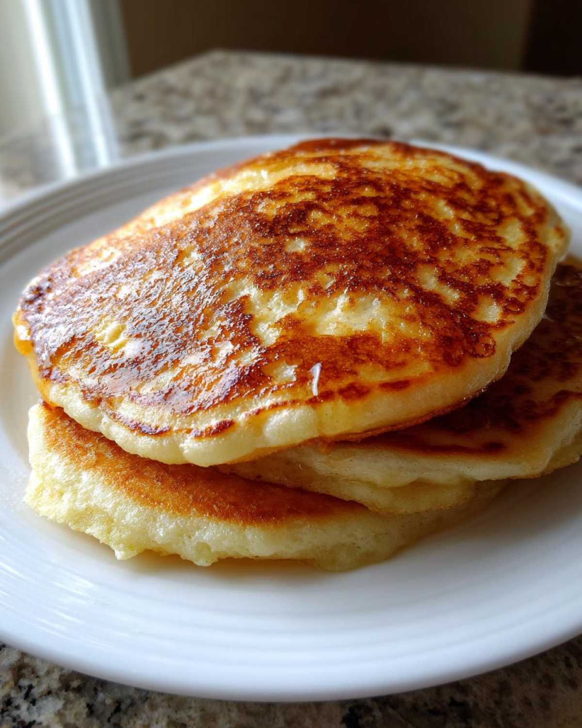 Close-up of three fluffy coconut flour pancakes stacked on a white plate.