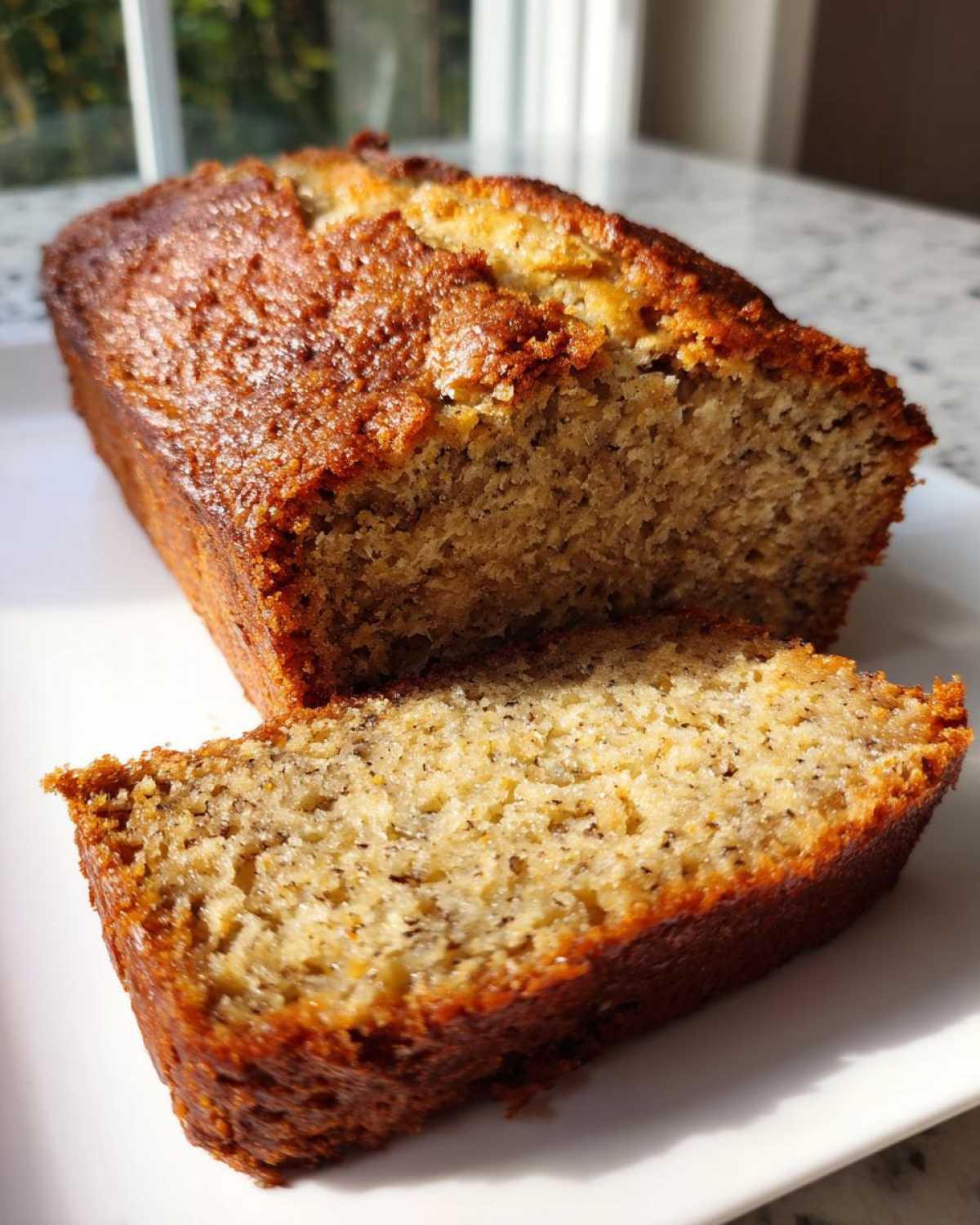 A loaf of greek yogurt banana bread with one thick slice cut and resting in front.