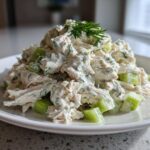 A mound of creamy greek yogurt chicken salad mixed with celery chunks and topped with fresh dill.