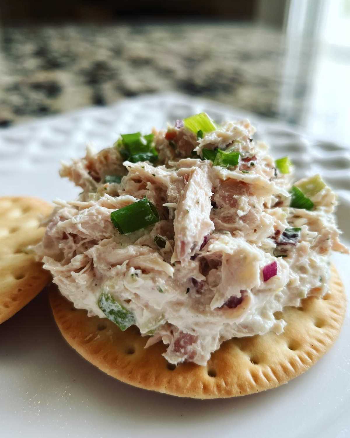 Close-up of a scoop of creamy ham salad recipe topped with chopped green onions on a round cracker.