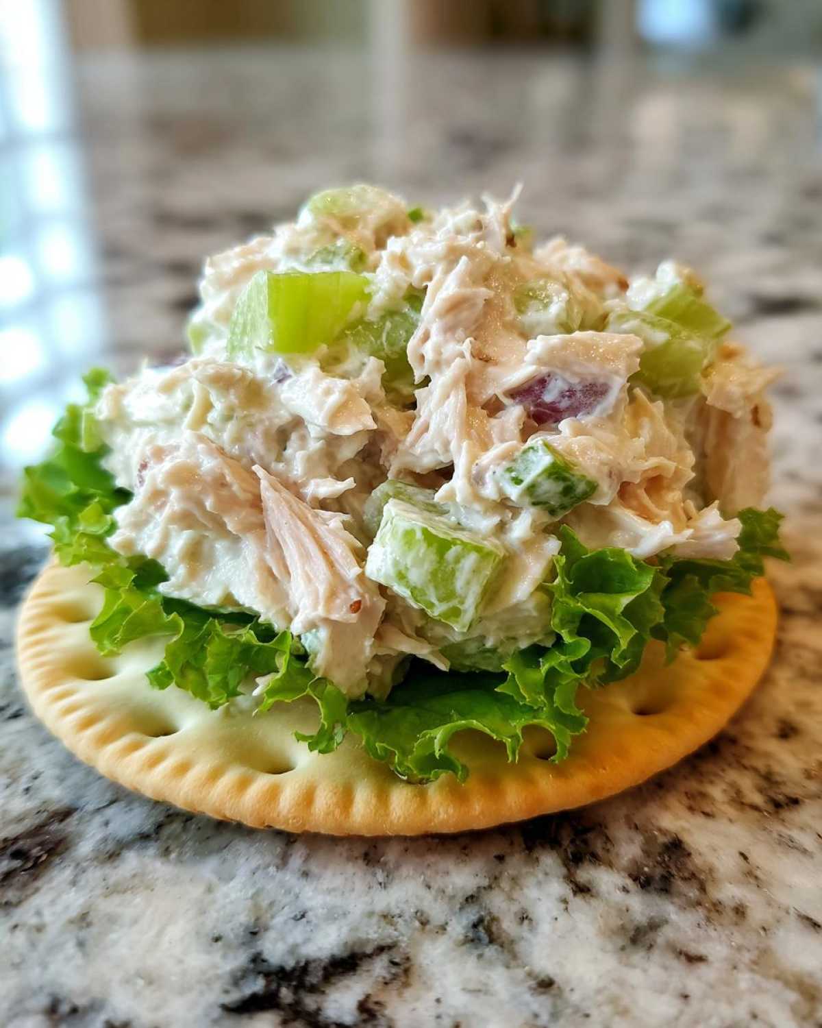 Close-up of a scoop of creamy ham salad recipe with celery served on lettuce atop a round cracker.